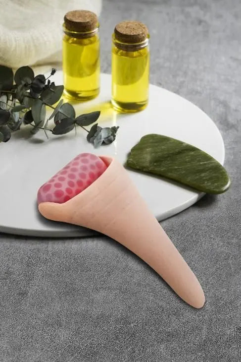Reduce puffiness ice roller in pink with a textured surface, alongside essential oils and a green massage tool